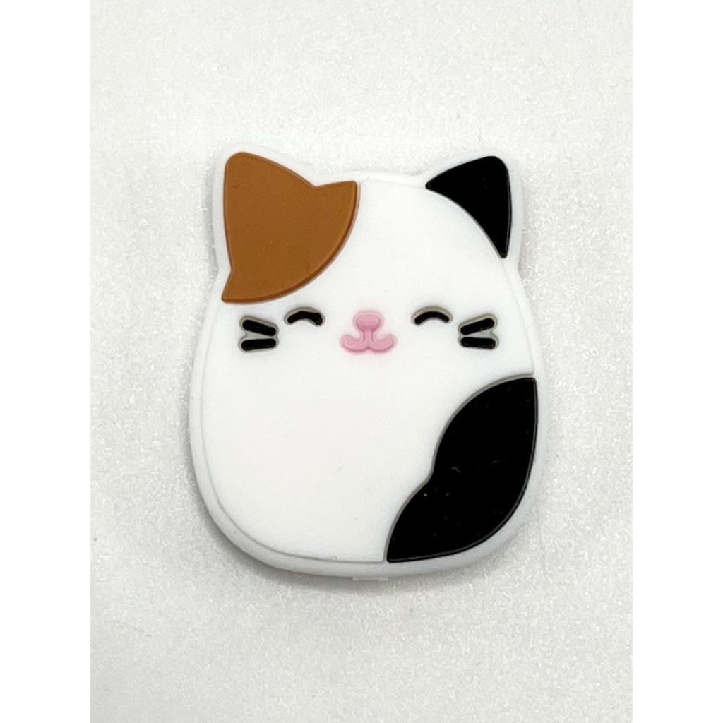 A silicone bead in the shape of a cute cat with black, white, and brown colors.