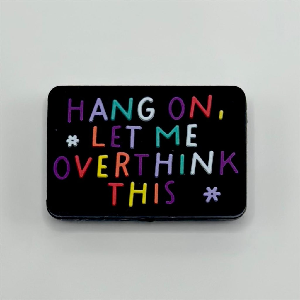 A rectangular silicone bead with the text 'HANG ON, LET ME OVERTHINK THIS' written in a colorful font on a black background.