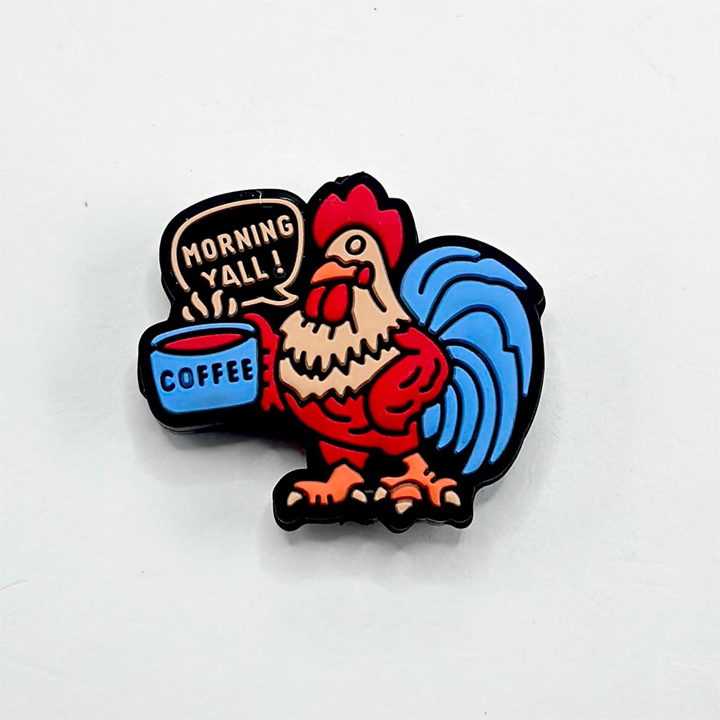 A silicone bead featuring a cartoon rooster with a blue tail feathers holding a cup of coffee and the text 'MORNING Y'ALL!'