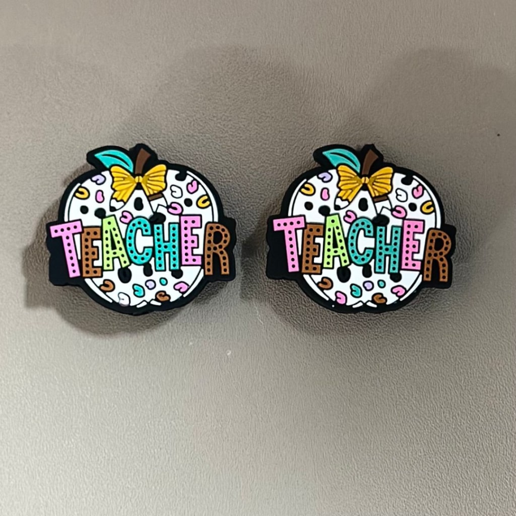 Two silicone beads with the word 'TEACHER' written on them, decorated with colorful letters and butterfly motifs.