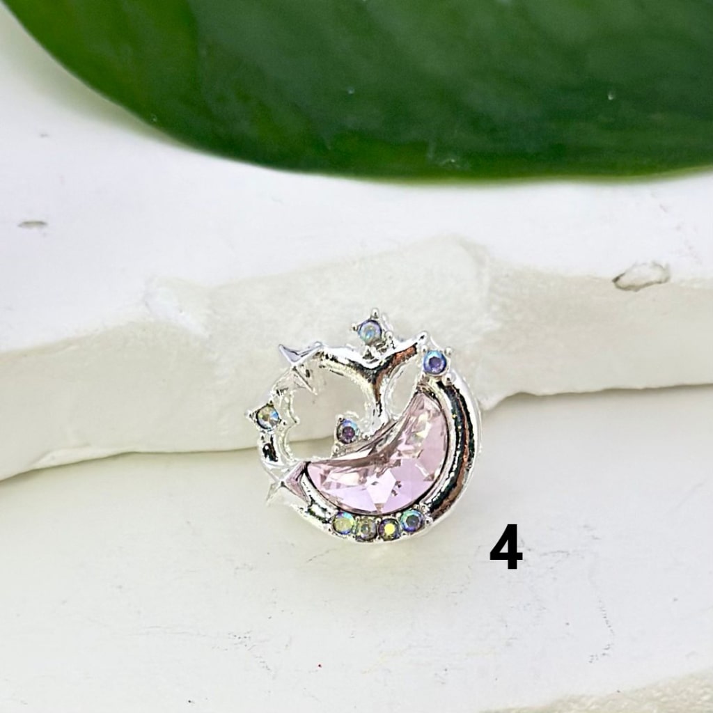 Silver alloy crescent moon and stars-shaped beads with colorful rhinestones, alongside a white pen for scale.