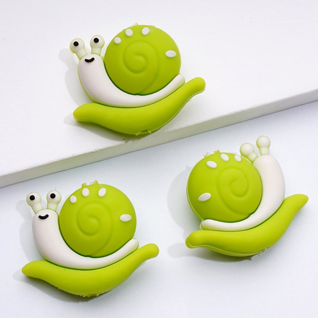 A collection of colorful silicone beads shaped like snails, with two in green and two in orange.