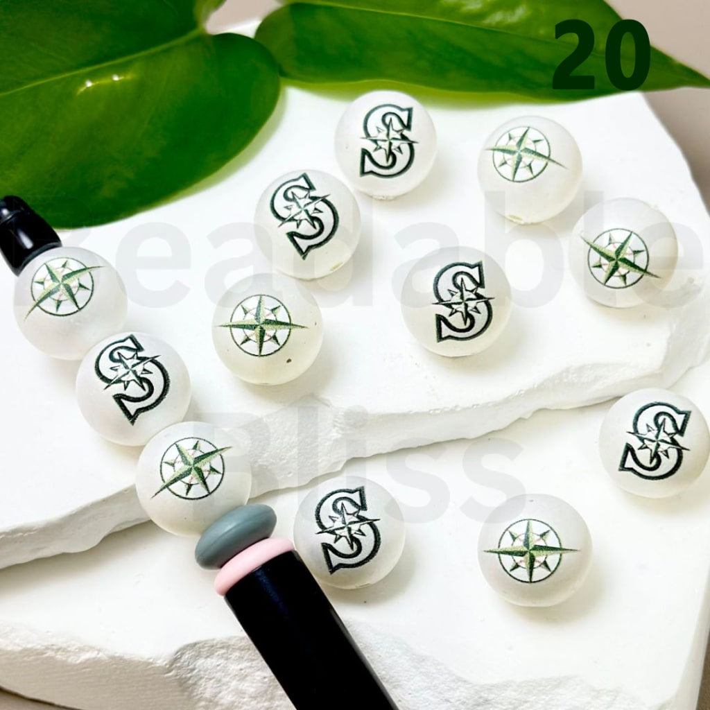 Set of white beads with black symbols on a white surface with green leaves in the background.