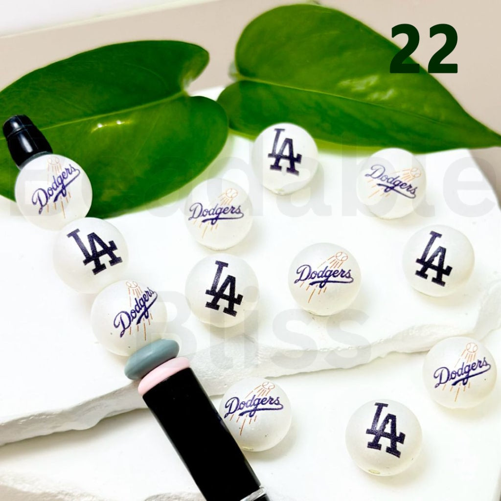 Set of Los Angeles Dodgers-themed lip glosses on a white surface with green leaves in the background.
