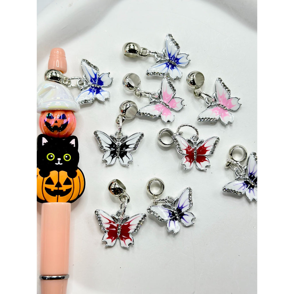 A selection of multicolored alloy charms shaped like butterflies with clear rhinestones, displayed alongside a pen for scale.