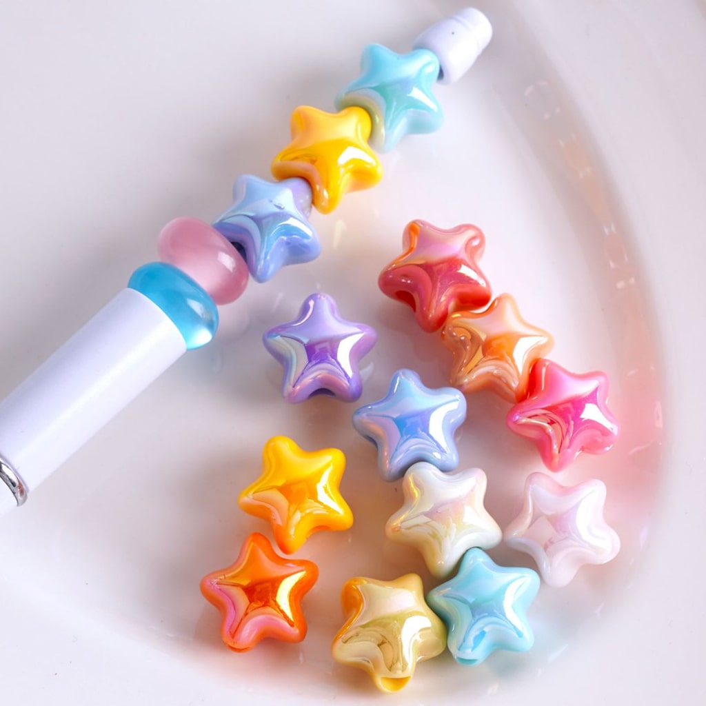 A collection of colorful, five-pointed star-shaped acrylic beads with a glossy finish. They are displayed alongside a tool, possibly for crafting or jewelry making.