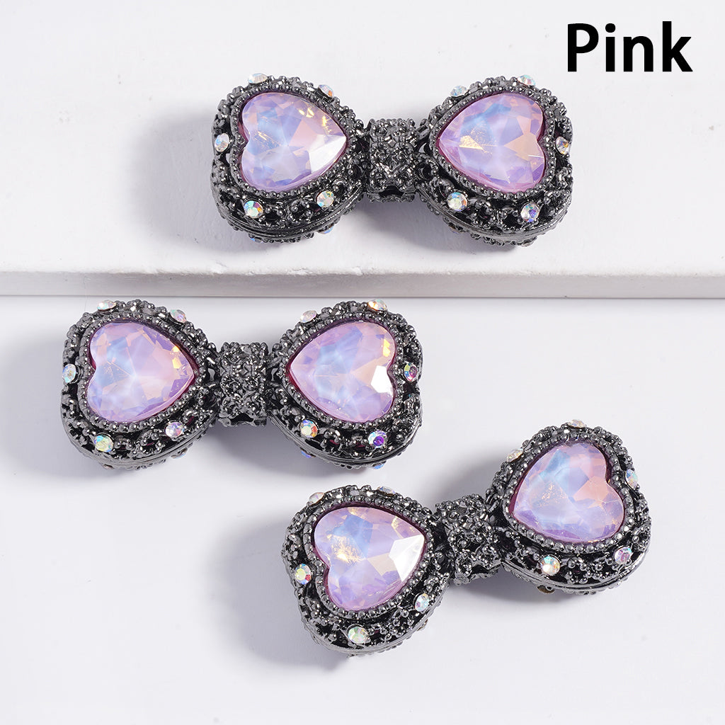 A collection of gun black bow-shaped hollow alloy acrylic beads with heart-shaped rhinestones, displayed alongside a pen for scale.