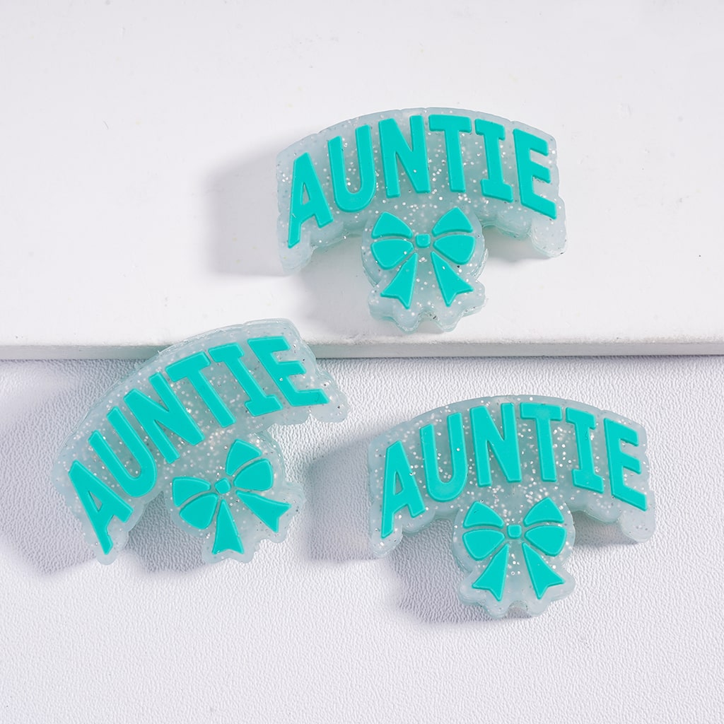 Three clear 'AUNTIE' wristbands with teal text and bows on a white background