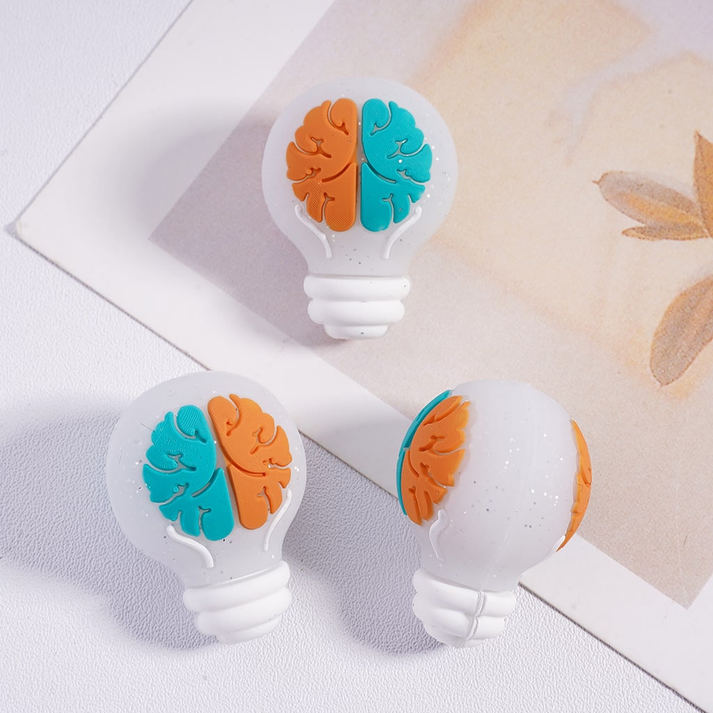 Three light bulb-shaped objects with orange and blue brain designs on a white surface.