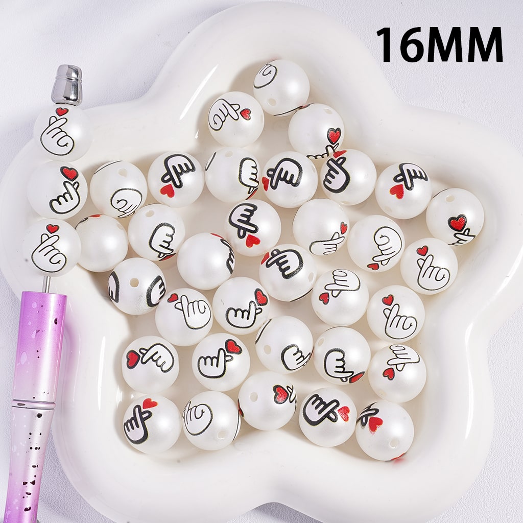 White beads with black designs on a white tray, with a pen on the side.