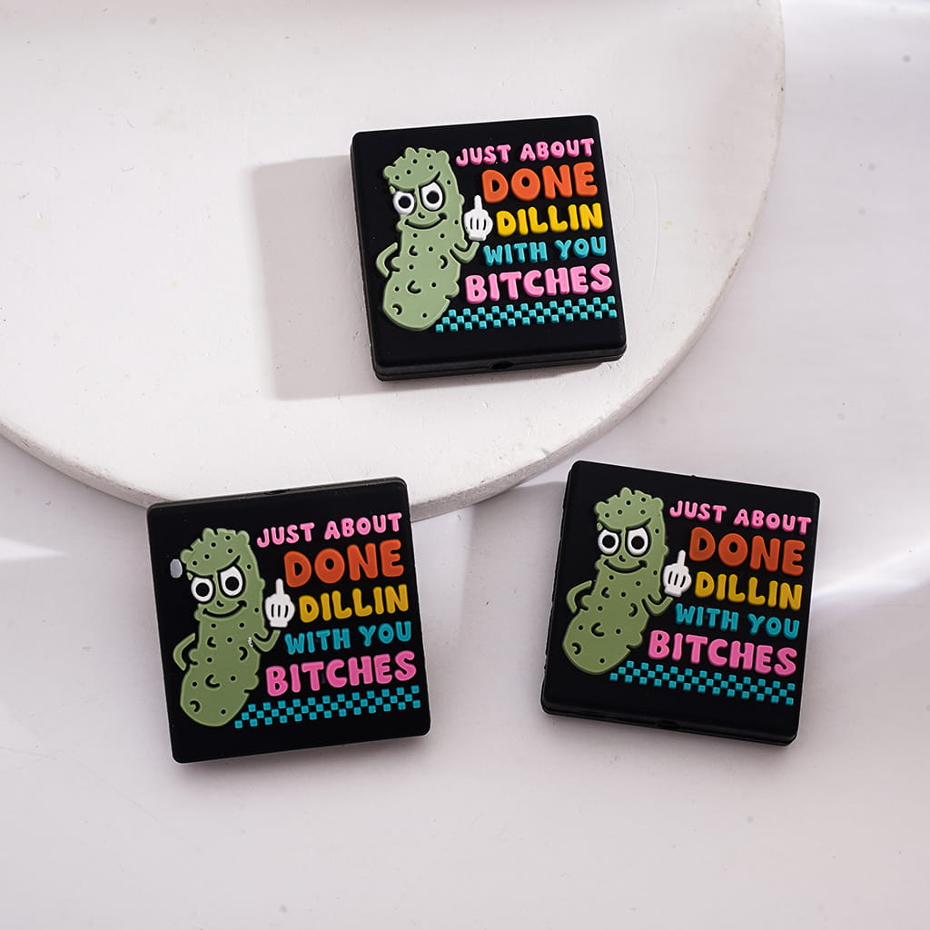 A silicone bead with text and a cartoonish character design in multicolor on a black background.