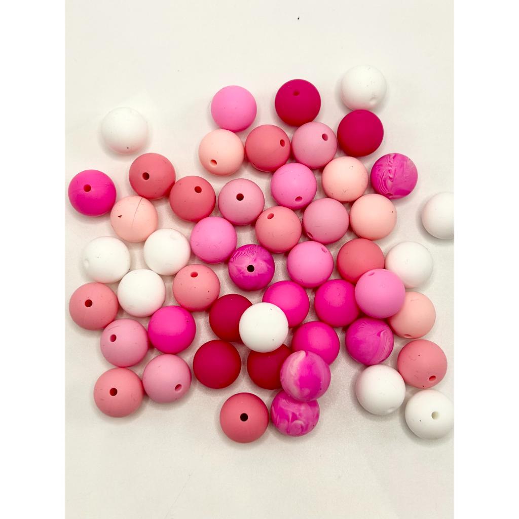 A collection of round silicone beads in various shades of pink, red, white, and purple with holes in the center for stringing.