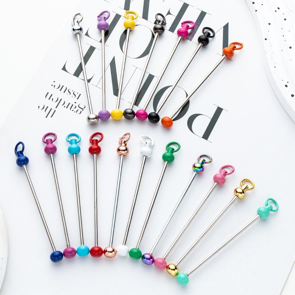 A collection of colorful keychain beadable bars with jump rings and keyring closures, displayed against a white background with a few beads lying in front of a magazine.