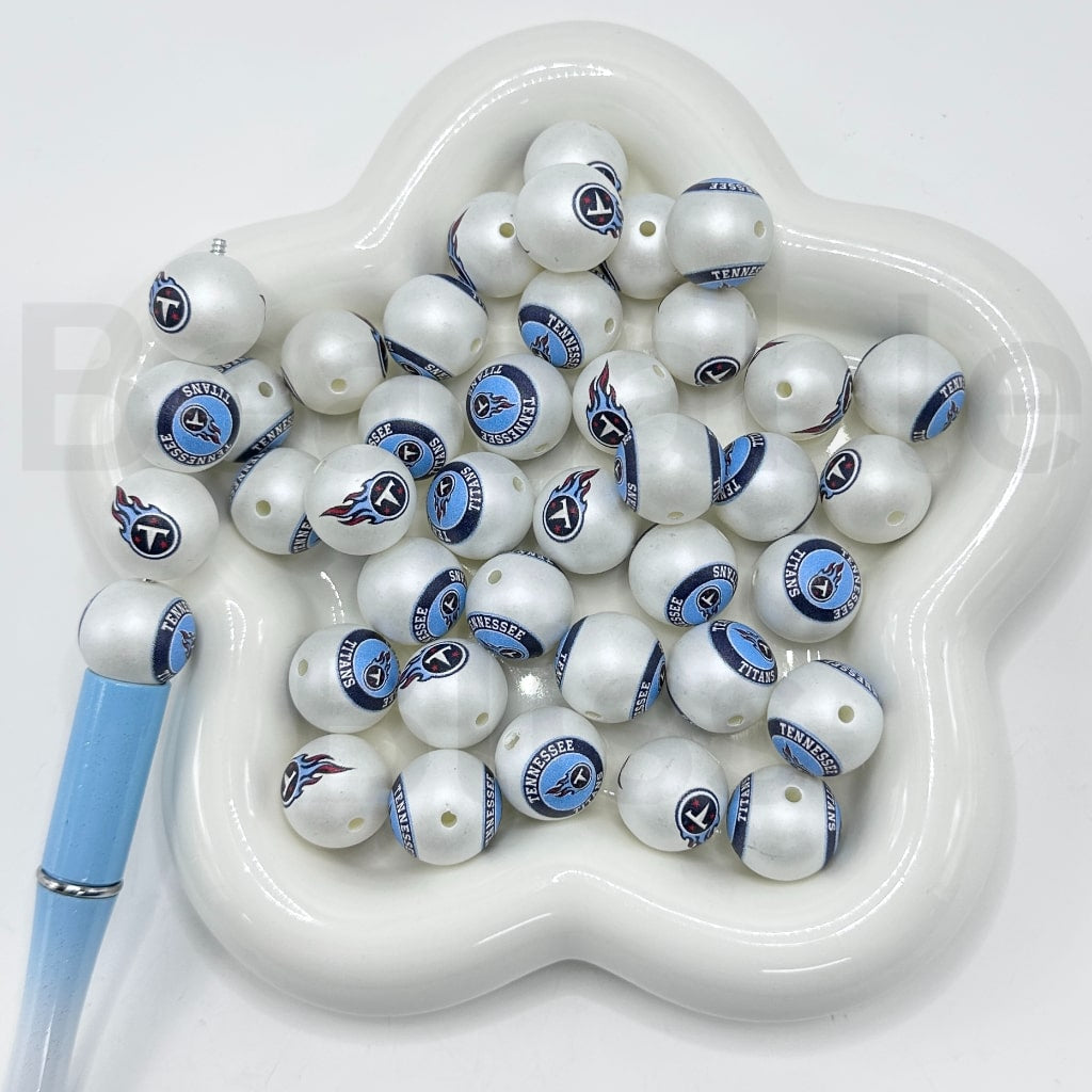 White beads with blue and black designs on a white dish with a blue pen
