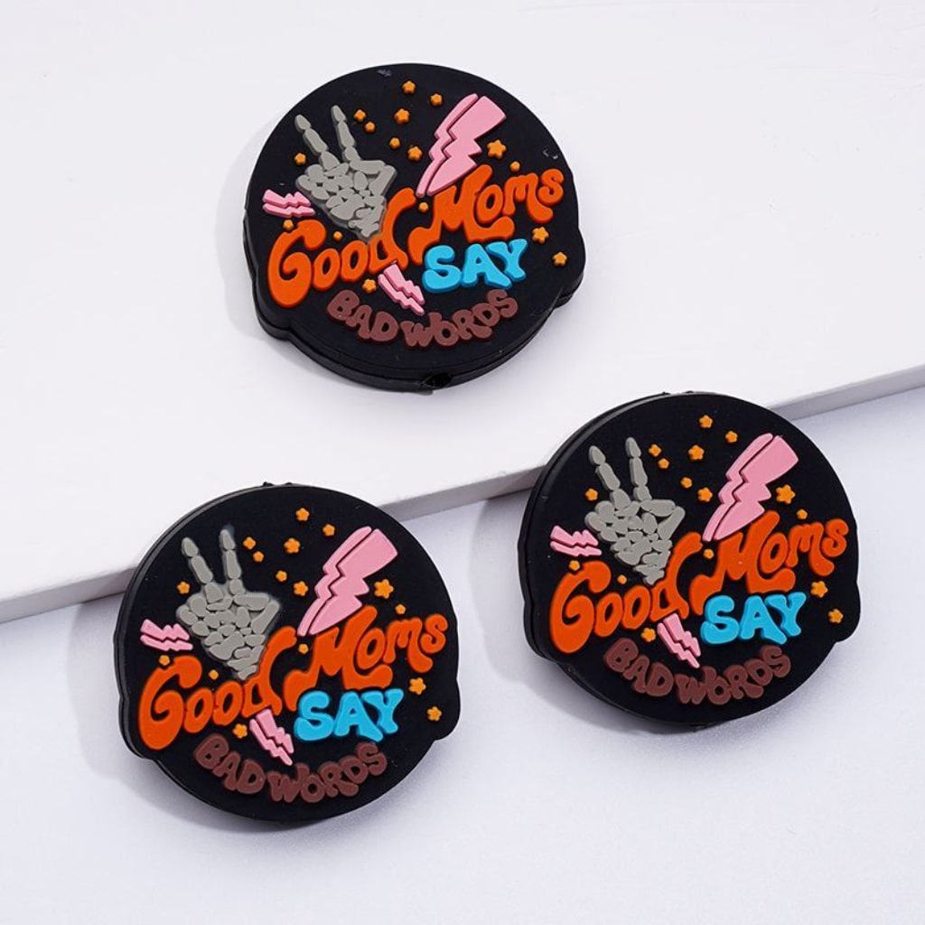 The image shows three round silicone beads with the phrase 'Good Moms Say Bad Words' printed on them, primarily in black color with multicolor text and decorative elements.