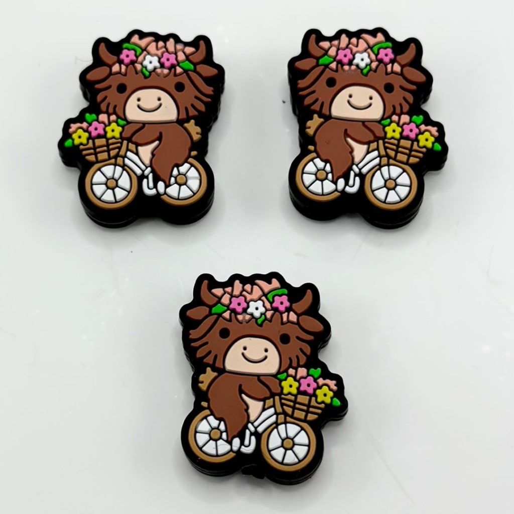 A set of silicone beads featuring a brown cow riding a bike with small flowers.