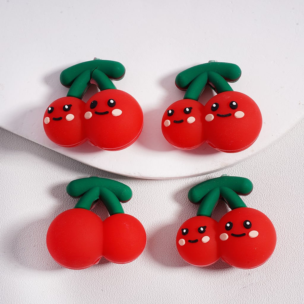 Two pairs of red cherry-shaped earrings with smiling faces on a white plate.