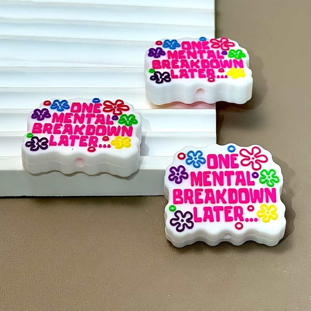 Silicone beads with the phrase 'One Mental Breakdown Later...' printed on them, adorned with colorful floral designs.