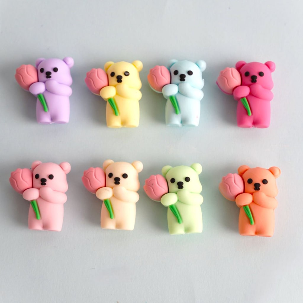 A collection of silicone beads in the shape of bears holding flowers in various pastel colors.
