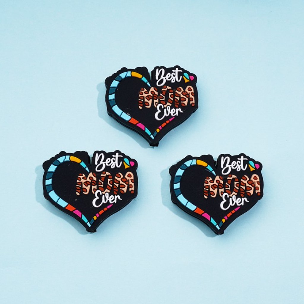 A set of three silicone beads in the shape of hearts with the phrase 'Best Mom Ever' printed on them, in multicolor design.