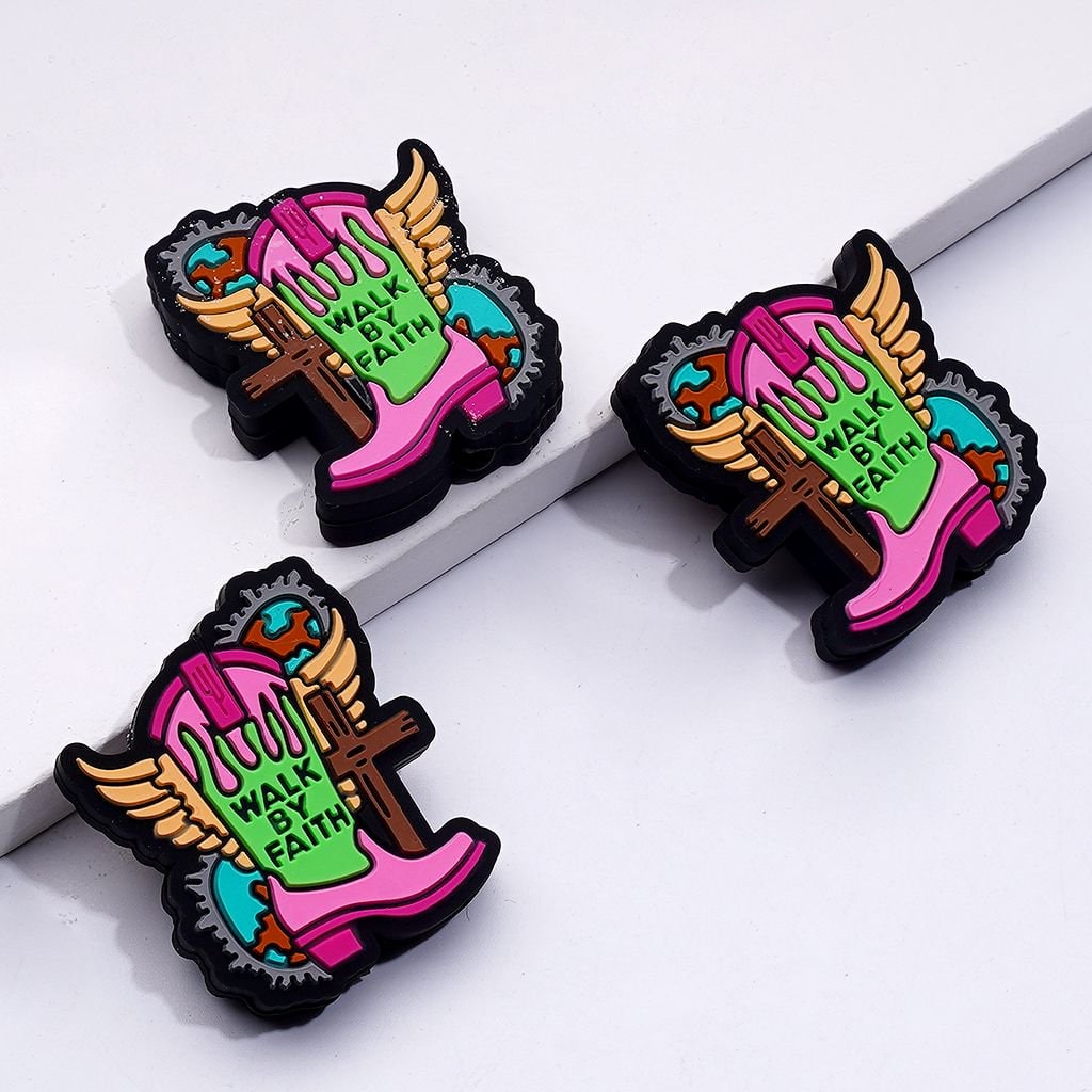 Three colorful boot-shaped pins with wings, cross, and 'Walk by Faith' text on a white background.