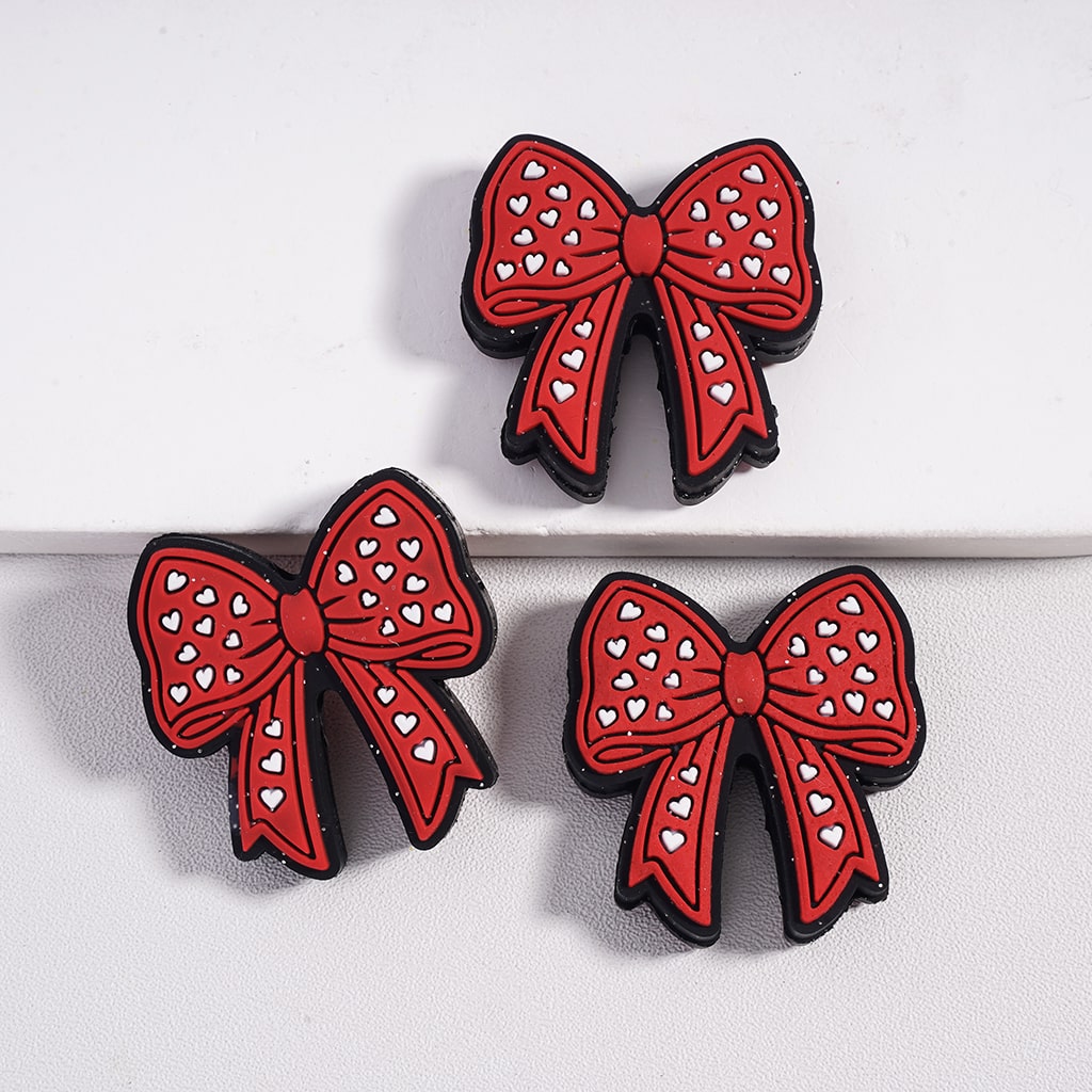 Three red bow-shaped cookies with white heart patterns on a light gray background