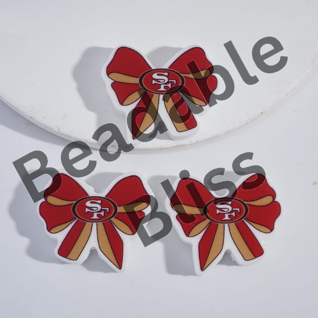 Red bow-shaped earrings with 'SF' logo on a white background, branded 'handsontupply'.com'.