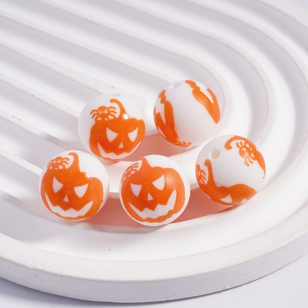 White and orange beads with pumpkin face designs on a white plate.