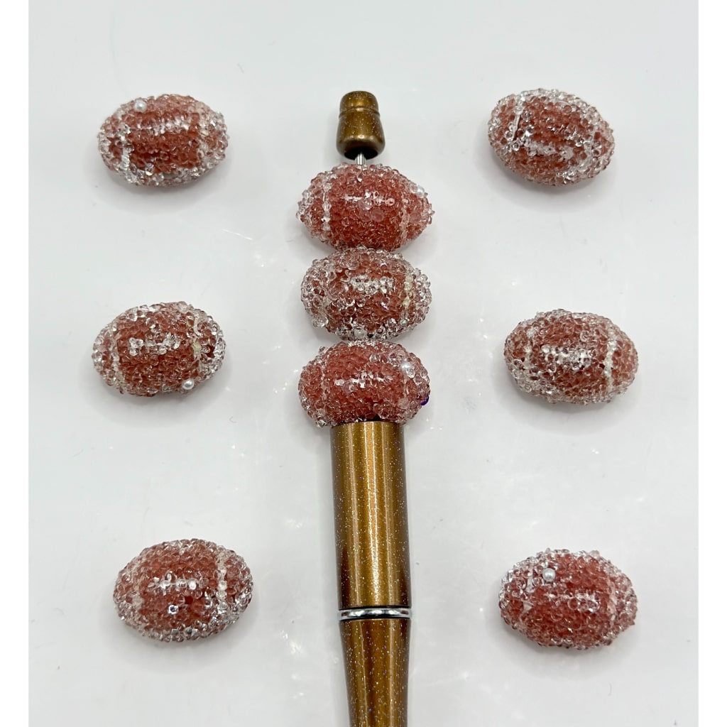 Acrylic beads in brown color with a design resembling a football, displayed alongside a tool for crafting.