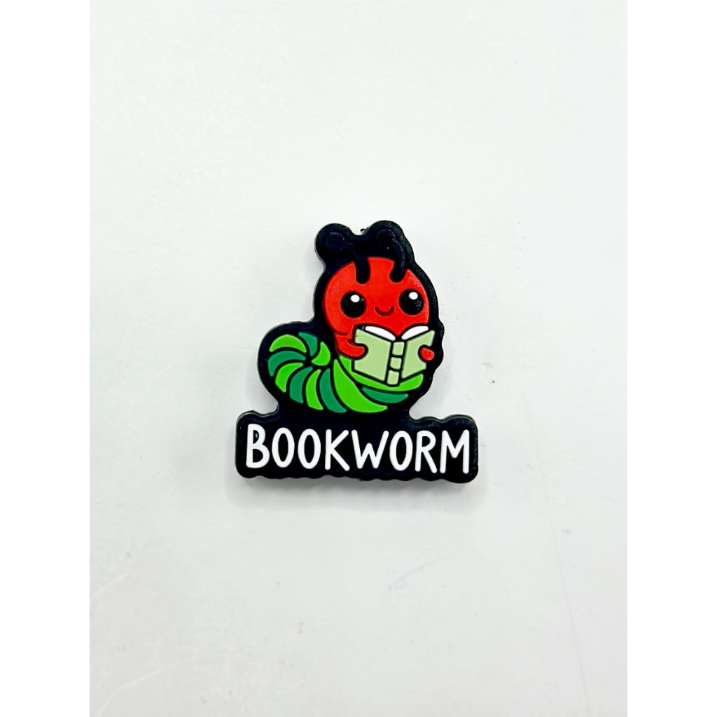 A silicone bead in the shape of a bookworm with a red body, green book in its mouth, and black details.