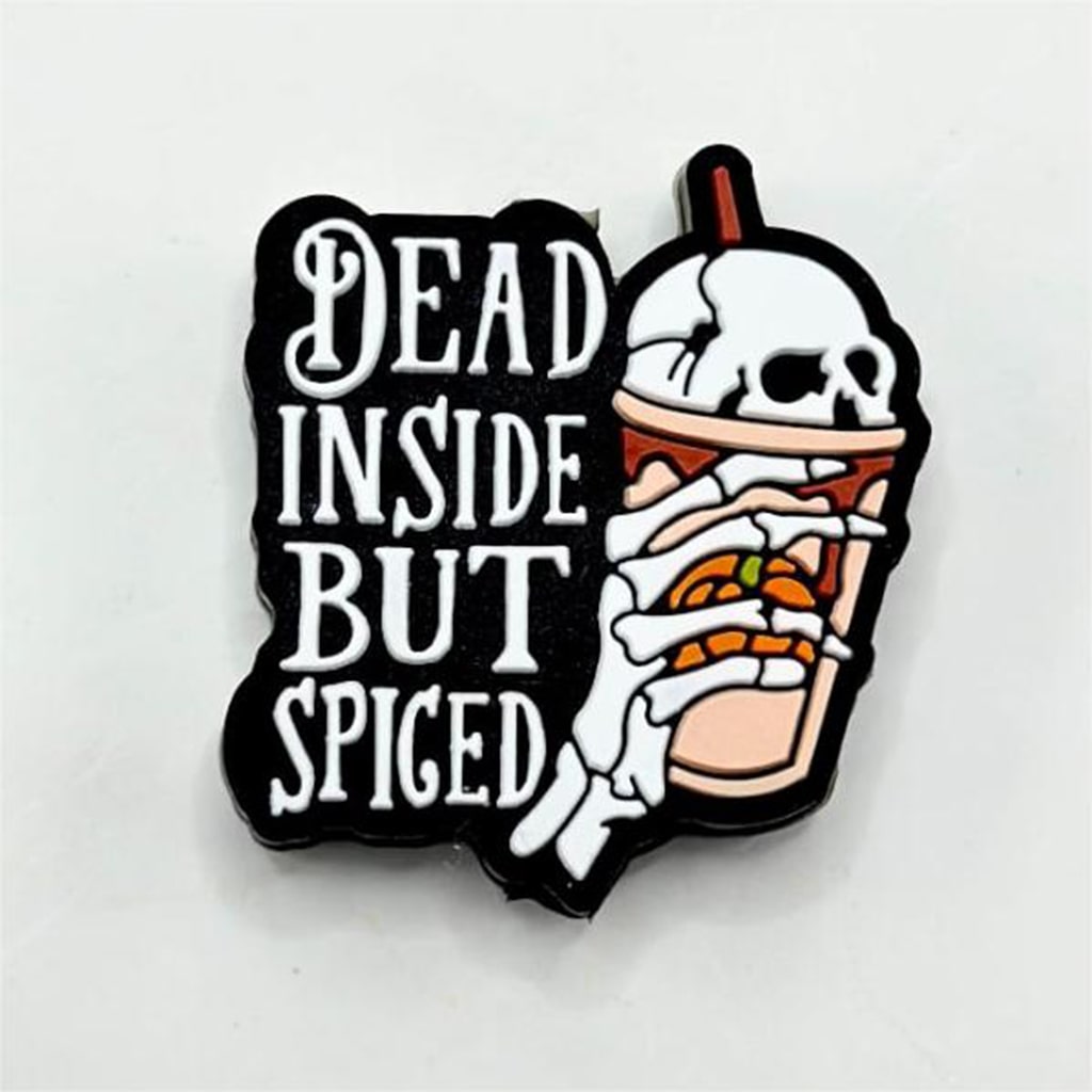 A pin with a design featuring a skeleton hand holding a drink with a pumpkin inside, accompanied by text 'DEAD INSIDE BUT SPICED'. The background is black, and the design is in white and orange.
