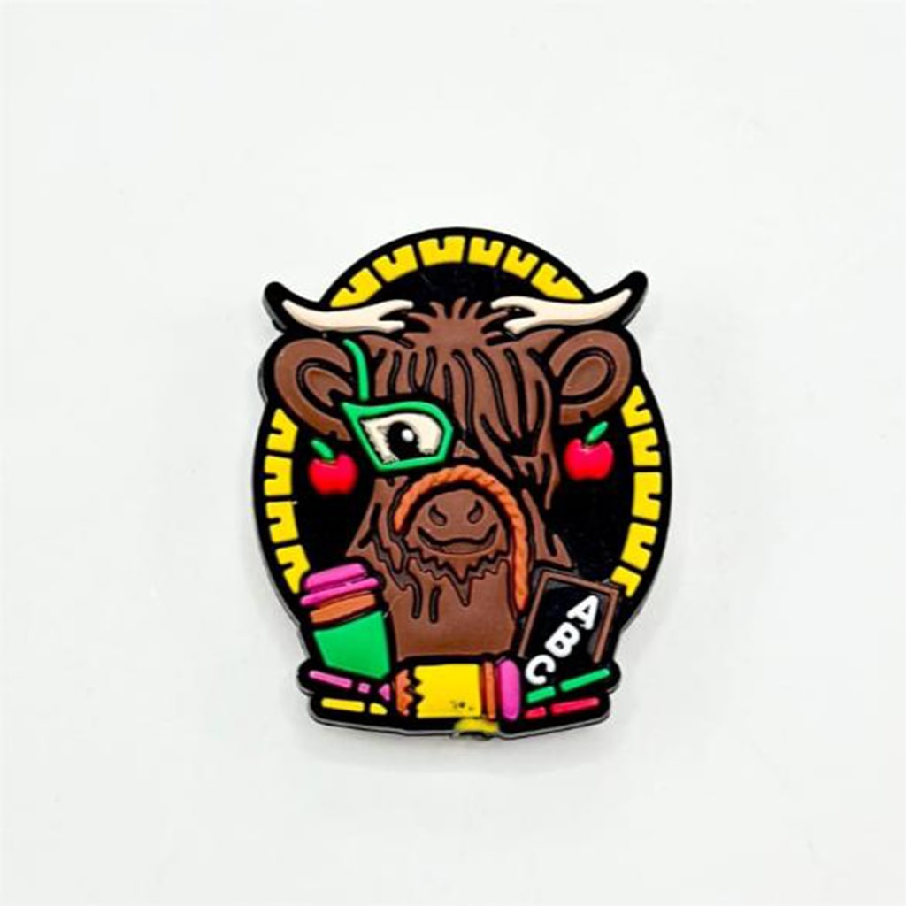 A silicone bead featuring a cartoon illustration of a Highland Cow with glasses and a book, predominantly brown in color with black and yellow accents.
