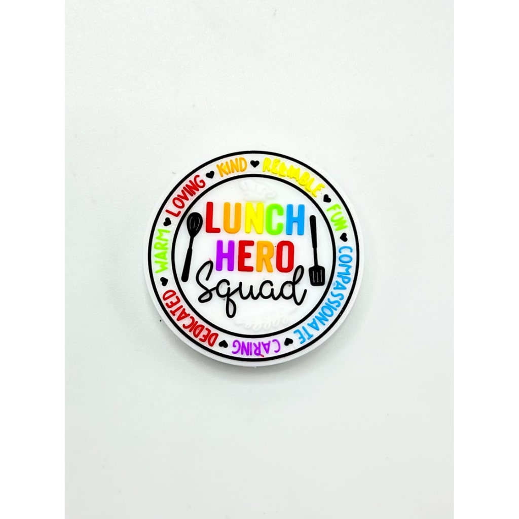 A round silicone bead with 'LUNCH HERO SQUAD' written in colorful letters and accompanied by illustrations of a water bottle, lunch box, and pen.