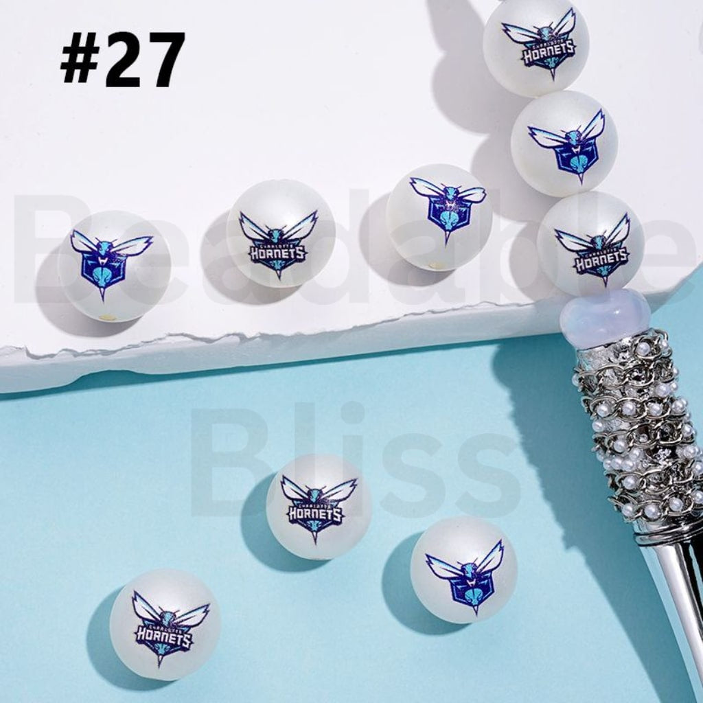 White golf balls with Hornets logo on a blue surface, with a decorative pen in the corner.