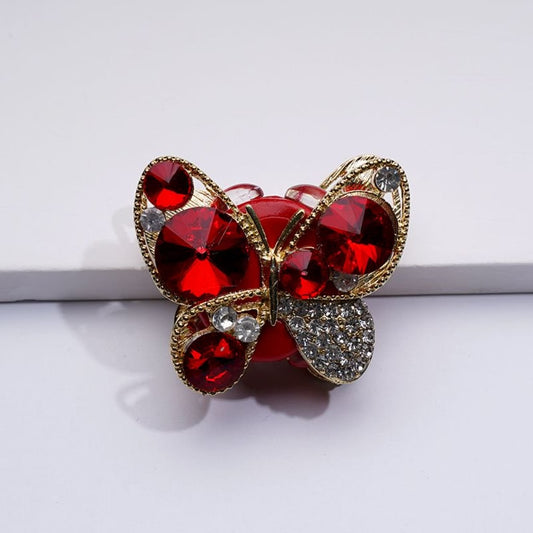 A gold alloy butterfly with red clear shiny rhinestones clay beads, against a white background.

