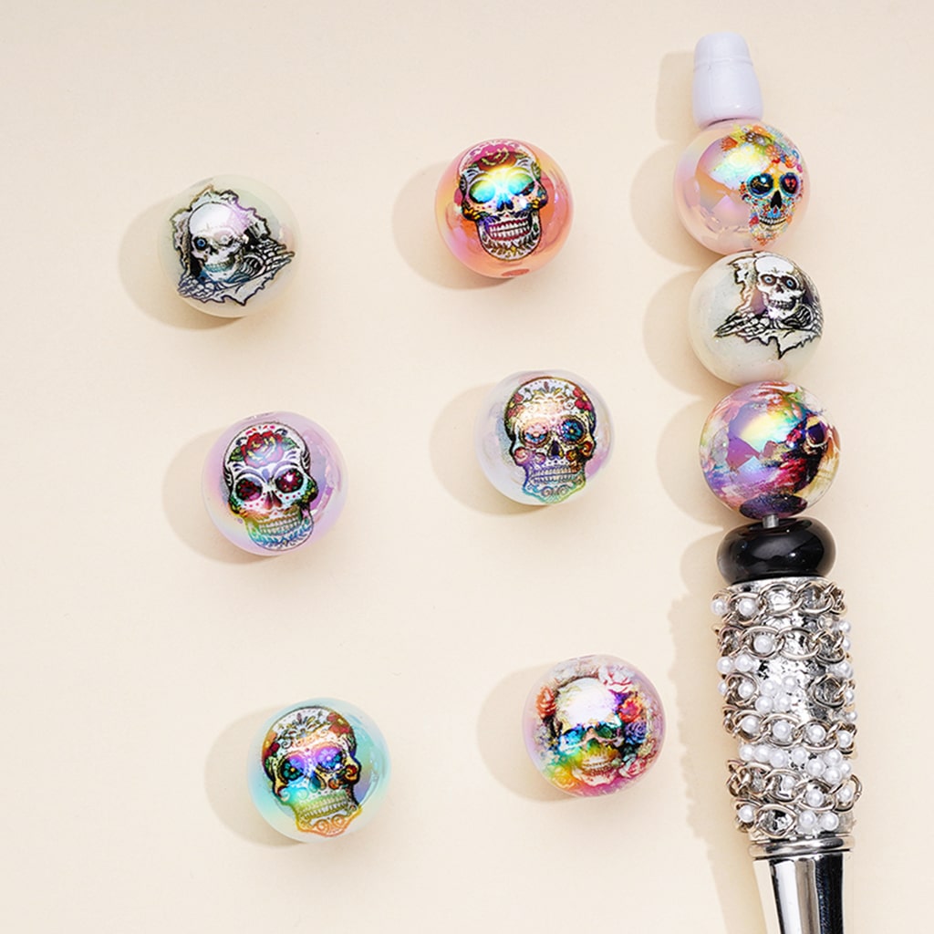 A collection of multicolored acrylic beads with skull designs displayed alongside a pen for scale.

