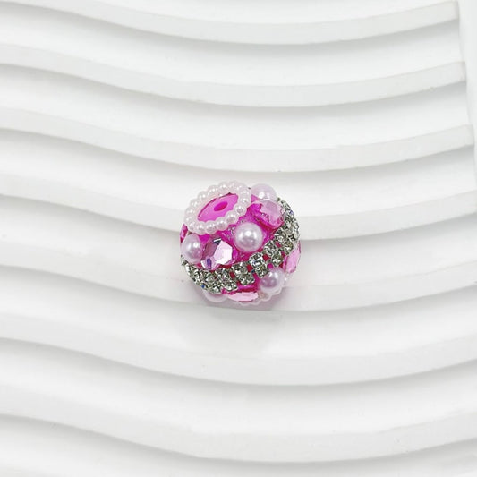 Decorative bead with pink and silver design on a white textured background