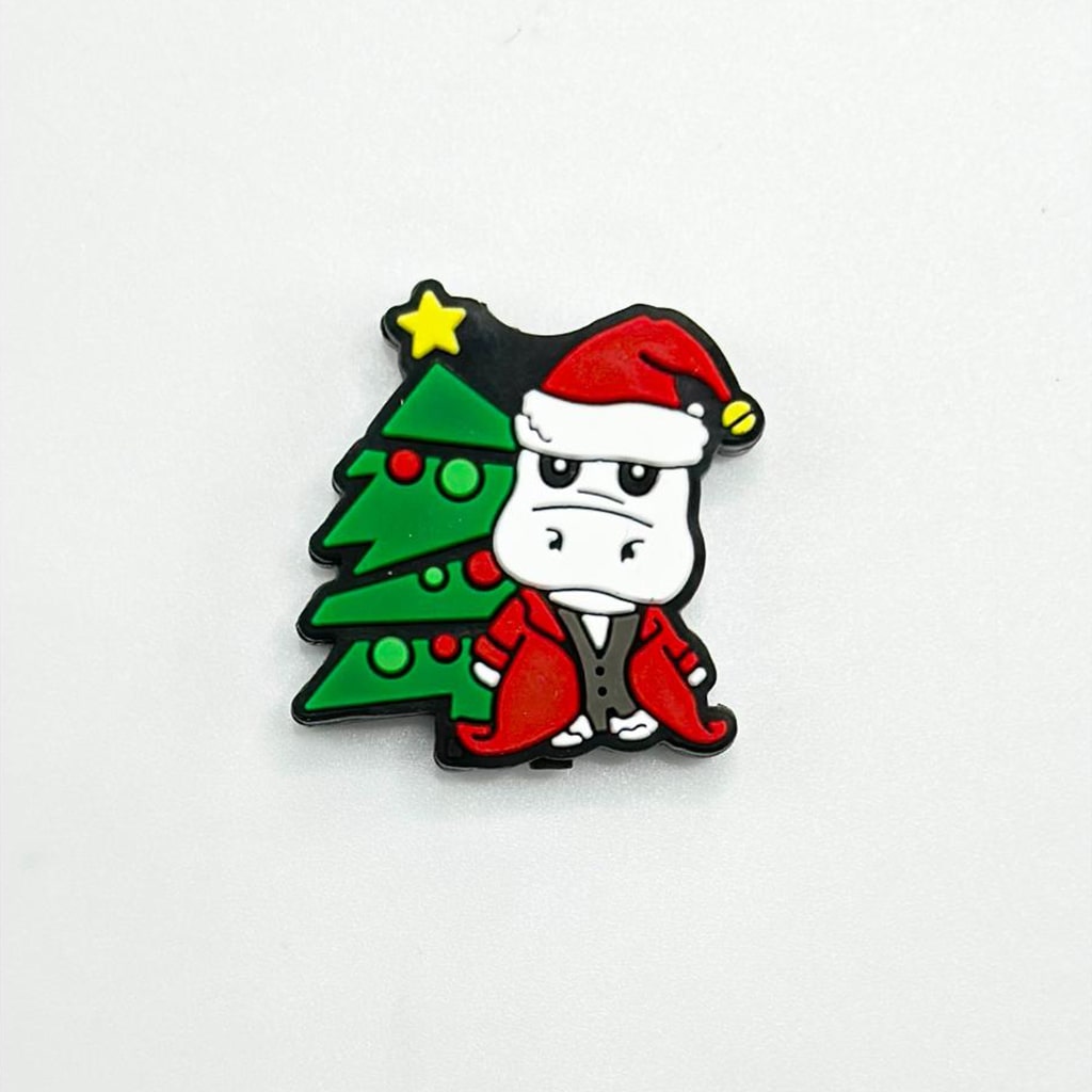 A silicone bead featuring a hippo wearing a Santa hat next to a Christmas tree, with a yellow star on top.


