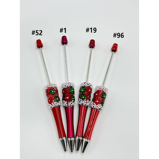 A collection of pens with red and green bead embellishments and white pearl tops, interspersed with clear rhinestones.

