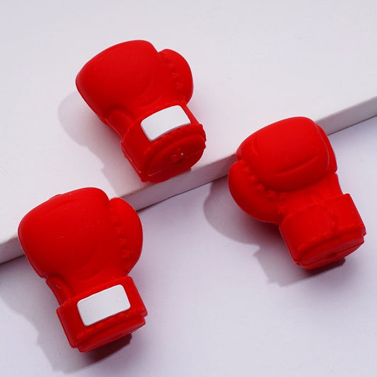 A collection of silicone beads in the shape of boxing gloves in black, red, and blue colors, displayed alongside pens for scale.

