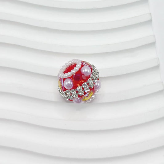 Decorative bead with red center, pearls, and crystals on a white background