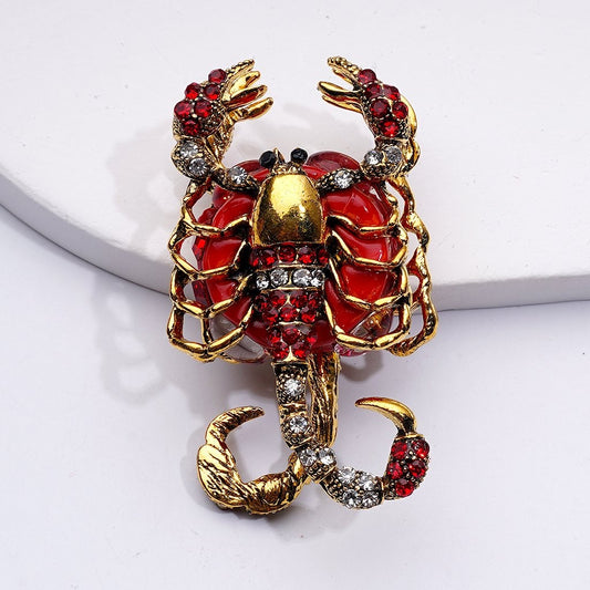 Scorpion-shaped brooch with red and gold details on a white background

