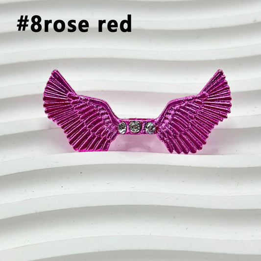 Assorted colorful angel wings with clear rhinestone spacers placed on a white surface.

