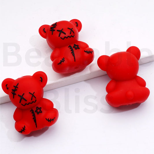 Three red teddy bear-shaped stress relievers with black markings on a white surface.

