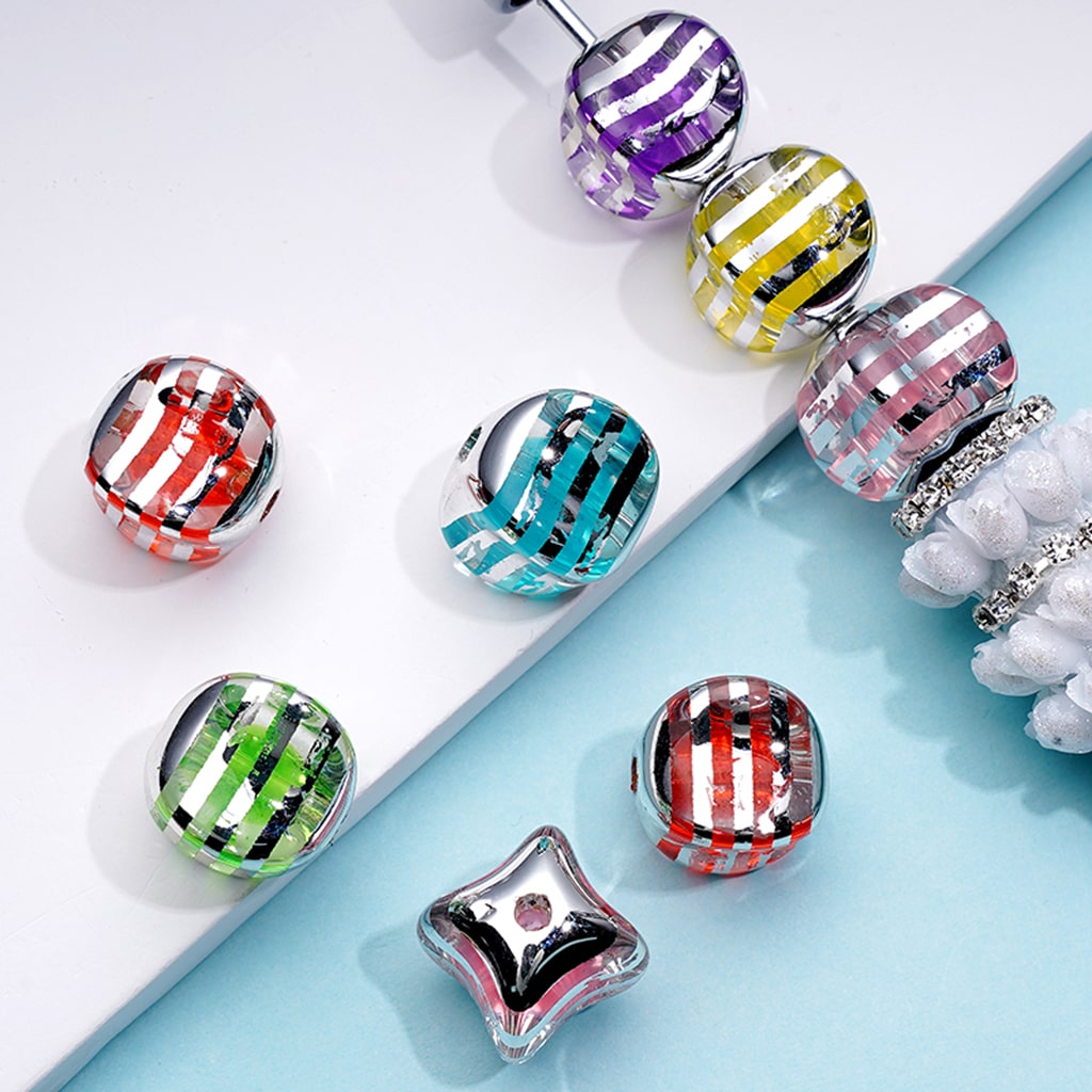 Colorful striped beads on a light blue surface with a white flower.


