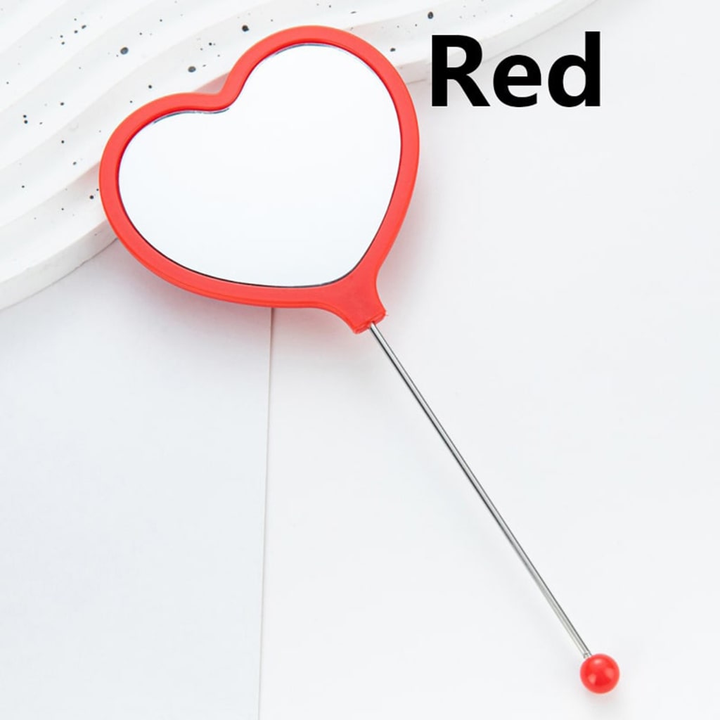 A collection of heart-shaped handheld makeup mirrors in various solid colors, each with a different color bead attached to the end.

