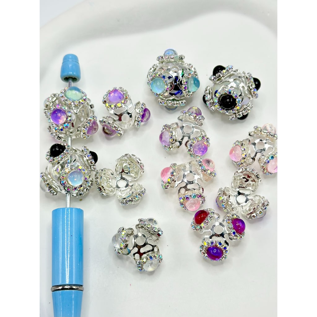 A collection of gold and silver bead caps with colorful rhinestones and large pearls designed for 16MM beads, displayed on a white surface.

