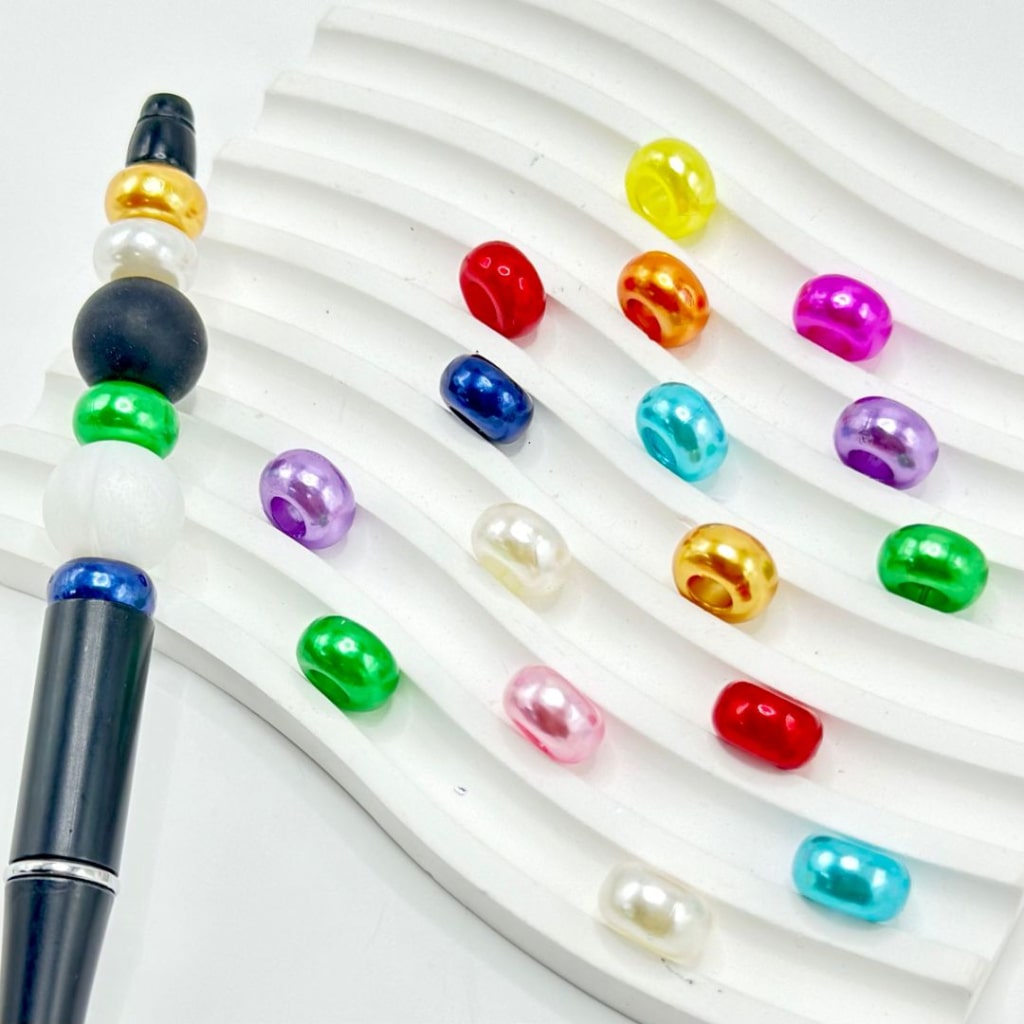 Assorted colorful acrylic beads with a large hole, displayed on a white surface, alongside a beadable pen.

