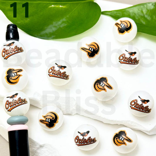 Collection of Baltimore Orioles-themed lip balms on a white surface with green leaves.


