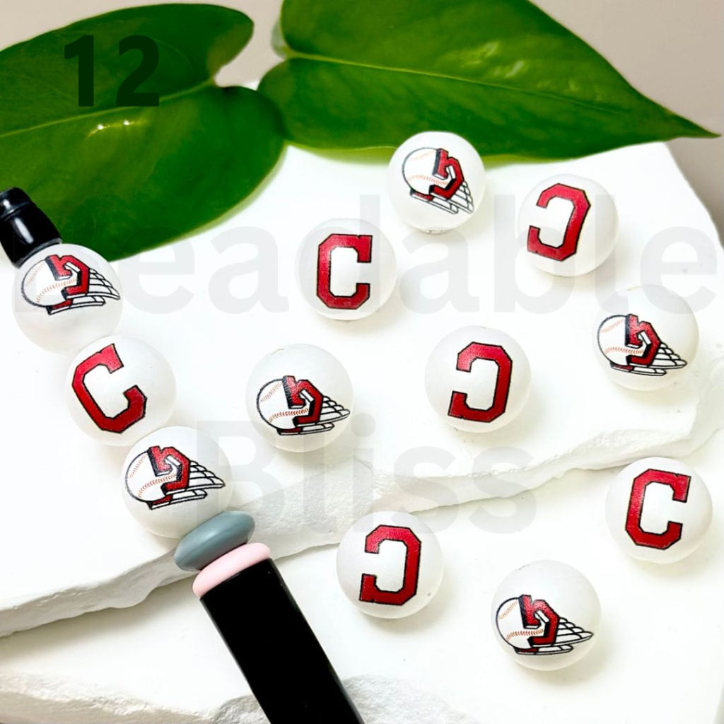 Set of white lip balm tubes with red and black designs on a white surface with green leaves in the background.


